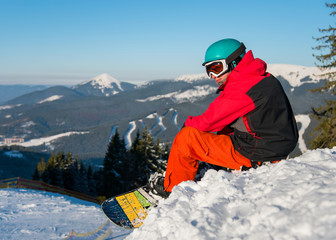 Fototapeta na wymiar Shot of a snowboarder enjoying beautiful view of snowy mountains, winter ski resort, relaxing on the edge of a slope looking around copyspace recreation travelling tourism.