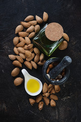 Almond oil and almond nuts on a dark brown stone background, high angle view
