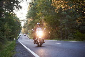 Bearded biker in sunglasses, helmet and black leather clothing riding modern powerful cruiser...