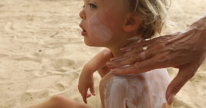 Mother applying sunscreen lotion on son back at beach. Mother preparing child for bath in sea