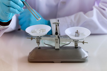 The doctor of medicine is weighing the medicines by vintage balance scale at the laboratory. Chemist hand using scales weighing with medicine in lab