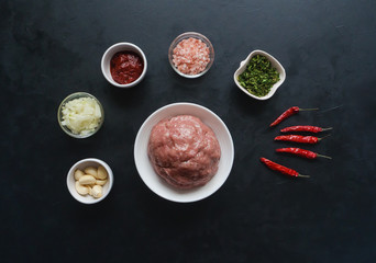 Minced meat and a set of ingredients for cooking on a black table.