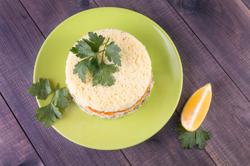 Layered round salad with vegetables and fish Mimosa on a plate on a wooden background. Top view