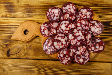 Sliced salami sausage on cutting board on wooden table. Top view