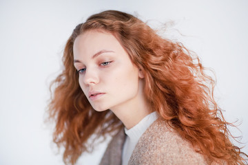 Beautiful girl dressed in french style on a white background. red hair woman is wrapped in a coat, winter clothes. Smiling lady wearing warm clothes, winter portrait