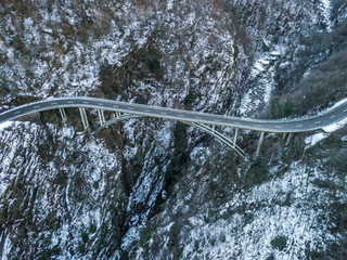 Aerial view of road bridge in Switzerland over a deep valley in winter with snow covered ground. Icy conditions.