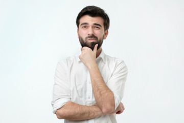 Portrait of a pensive spanish man in white shirt against a white background. He is trying to make a...
