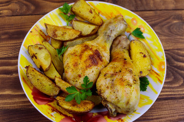 Baked chicken drumsticks with potatoes in a plate on wooden table