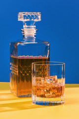 glass of whiskey with ice and decanter full side view blue and yellow