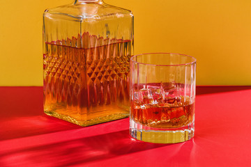 glass of whiskey and ice on red and yellow background with decanter