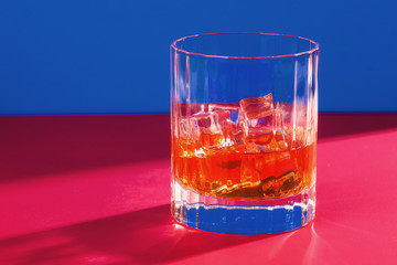 glass of whiskey with ice on blue and red background