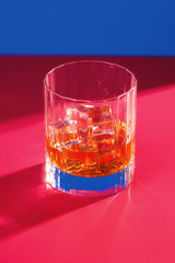 whiskey glass with ice on blue and red background vertical