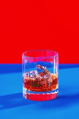 whiskey glass with ice on blue and red background vertical mid crop