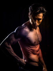 Handsome muscular shirtless young man standing confident, front view, looking away