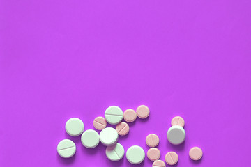 Pink and white pills scattered on a purple background. Copy space for text