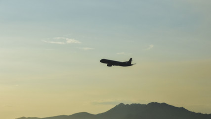 silhouette of an airplane flying over the mountains against a clear sky