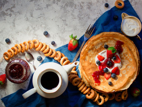Overhead stack of thin pancakes poured with sour cream and decorated with fresh strawberries and blueberries. The concept of Russian tea party at holiday Maslenitsa, Shrovetide