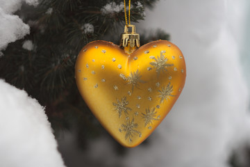 Christmas decoration in the form of a golden heart with patterns on the background of snow-covered coniferous tree close-up