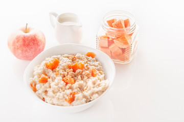 Fototapeta na wymiar Oatmeal with pumpkin and nuts in a plate, an apple, sliced carrots in a jar and a jug of milk on a white background. Close-up.