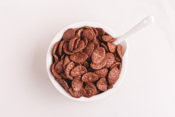 Crunchy chocolate corn flakes in bowl on light marble background