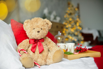 Two teddy bears siting on the bed with red candys near christmas tree.