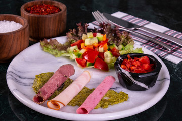 Meat plate with thinly sliced salami and jamon with salad on the marble background