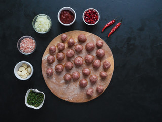 Meat meatballs and a set of ingredients are laid out on a black table.