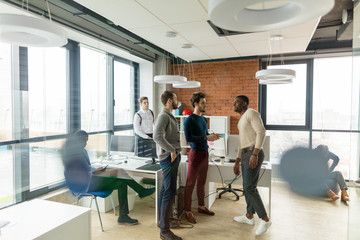 Successful mixed race hipster male team in coworking space. Freelancers cooperate working in open space modern office