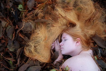 Portrait einer nackten jungen reizenden sexy Frau auf Herbstlaub liegend, die langen rotblonden...