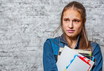 portrait of young teenager brunette girl with long hair holding books and note books wearing backpack on gray wall background