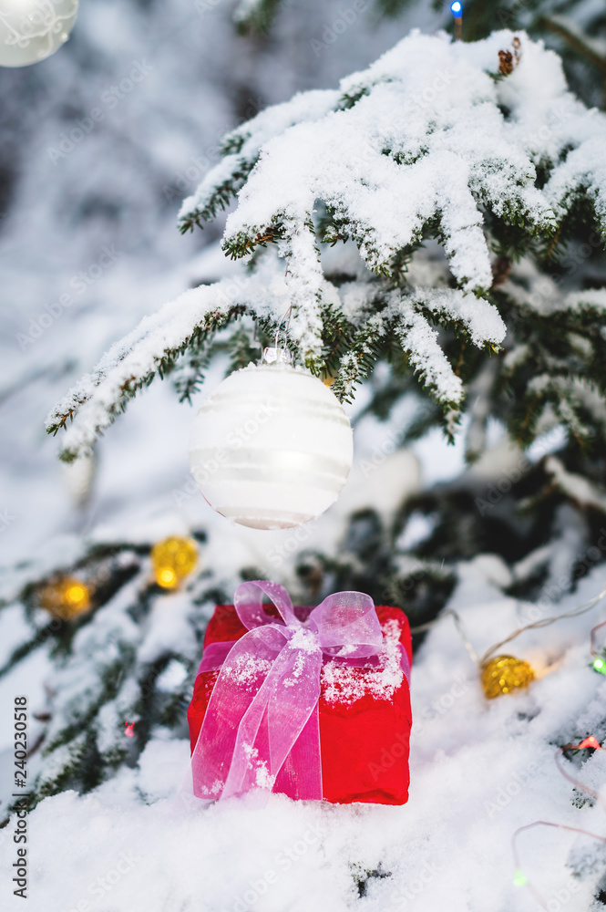 Wall mural close-up red new year's gift with a white ribbon next to christmas toys on the branches of a snow-co