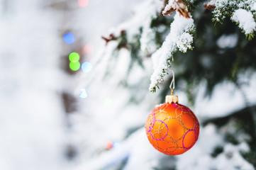 Close-up of a Christmas toy on a snow-covered lively tree in the winter forest on the background of lights