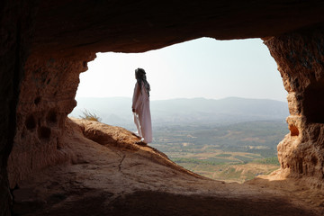 ISOLATED ARABIC MAN WITH DJELLABA AND TURBAN LOOKING TO SUNRISE FROM A CAVE