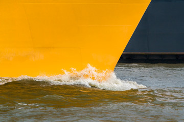 A yellow ship's bow in motion in the harbor. 