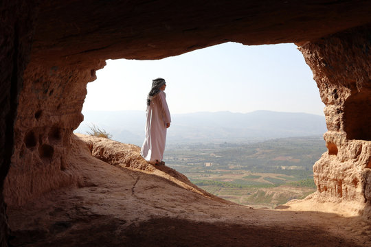 ARABIC MAN LOOKING AT THE VALLEY FROM THE ENTRANCE OF A CAVE