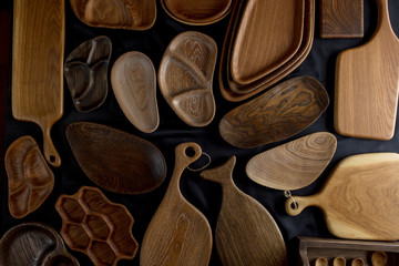 Top view of unused brand new brown handmade wooden kitchen utensil, made from different wood species, dish plate and cutting board on black background