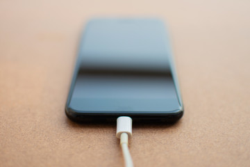 Charging battery mobile phone with blank screen on the wooden table. Selective focus..