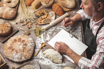 Portrait of smiling Baker's hands chef writing a new recipe of homemade bread on white paper shift,...