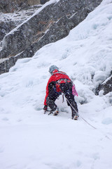 Fototapeta na wymiar male ice climber in heavy snowfall and bad weather climbing a frozen waterfall in the Swiss Alps