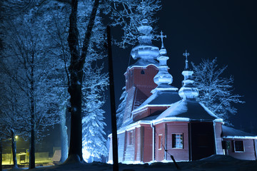 Beautiful illuminated wooden church photography  in the night  winter full of snow Tylicz Poland