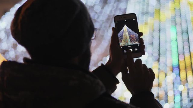 Rear view: Bearded man taking pictures of European Christmas market scene on smartphone. Close-up video