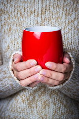 Girl in a light sweater holding a red cup of coffee