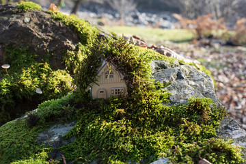 Christmas and New Year miniature house at forest in the sunlight. Little toy house close up. Festive background. Christmas decorations. Holiday and celebration concept.