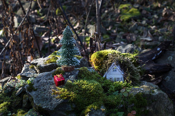 Christmas and New Year miniature house at forest in the sunlight. Little toy house close up. Festive background. Christmas decorations. Holiday and celebration concept.