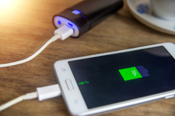 closeup of a powerbank charging a smartphone placed on a wooden table next to a cup of coffee