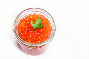 Red caviar in glass bowl on white wooden background