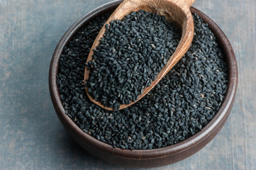 Black cumin seeds in bowl and wooden shovel or spoon. Organic herbal medicine for many diseases
