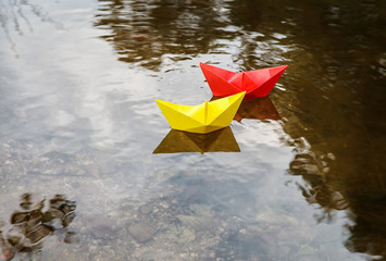 two multicolored paper boats floating on a stream