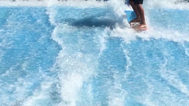 Unrecognizable young man flowriding and flowboarding on artificial sheet waves. The water flows up and over surfaces engineered to replicate the shape of ocean waves.