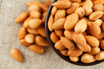 Almonds in a wooden cup on a burlap cloth background.